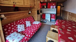 Een gezellig chalet-achtig vertrek met een houten bank, een kleine tafel en een kitchenette op de achtergrond.