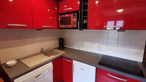 Een keuken met rode kastjes, een magnetron, een vaatwasser en een spoelbak.
