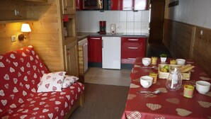 Een knus vertrek met een rode bank met hartjesprint, een kleine eettafel gedekt met kopjes en een mand met brood.