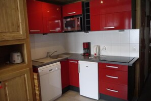 A compact kitchen with red cabinetry, a built-in microwave, a coffee maker, and a dishwasher. - 10m from ski slopes, 1st floor, view ski slopes, balcony, 32m², Méribel-Mottaret (Méribel - Les Allues)