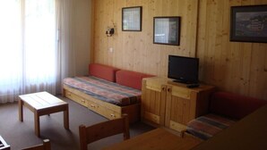 A cozy room with a wooden wall, a sofa, a television, and a small table.