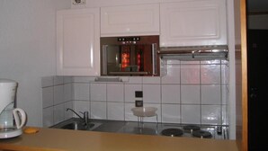 Una cocina compacta con armarios blancos, un lavamanos de acero inoxidable y un horno empotrado.