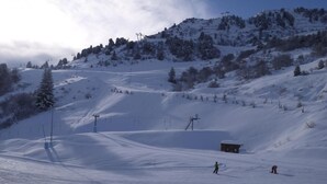 Una pista de esquí nevada con remontes, una cabaña pequeña y cielo despejado.