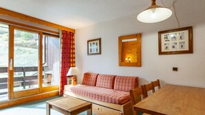 Um quarto acolhedor com sofá de madeira, mesa de jantar de madeira e uma janela grande com cortinas.