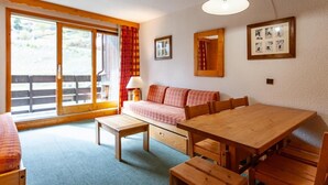 Um quarto acolhedor com uma mesa de madeira e bancos, um sofá e uma janela grande com cortinas.