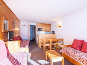 Ein gemütliches Zimmer mit einem Bett, einem Holztisch und einer Couch. Es gibt eine Küchenzeile mit Holzschränken und einer Mikrowelle.