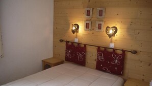 A bedroom with a wooden headboard, a bed with a white quilt, and two nightstands with red patterned curtains. - 150m from shops, 5th floor, balcony, ski locker, 40m², Méribel-Mottaret (Méribel - Les Allues)