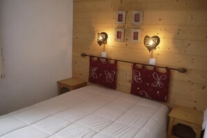 A bedroom with a wooden headboard, a bed with a white quilt, and two nightstands with red patterned curtains. - 150m from shops, 5th floor, balcony, ski locker, 40m², Méribel-Mottaret (Méribel - Les Allues)