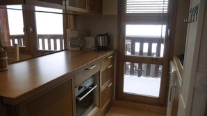 A compact kitchen with wooden cabinets, a built-in oven, a coffee maker, and a view through a glass door. - 150m from shops, 5th floor, balcony, ski locker, 40m², Méribel-Mottaret (Méribel - Les Allues)