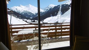 A room with a large window overlooking a snowy mountain landscape, including a ski lift and a wooden deck with chairs and tables. - 20m from ski slopes, 8th floor, view mountain, balcony, ski locker, 32m², Méribel-Mottaret (Méribel - Les Allues)
