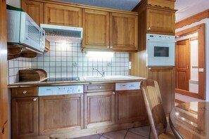 A kitchen with wooden cabinets, a built-in microwave, a dishwasher, and a stove. - 350m from ski slopes, balcony, tv, 40m², Méribel-Mottaret (Méribel - Les Allues)