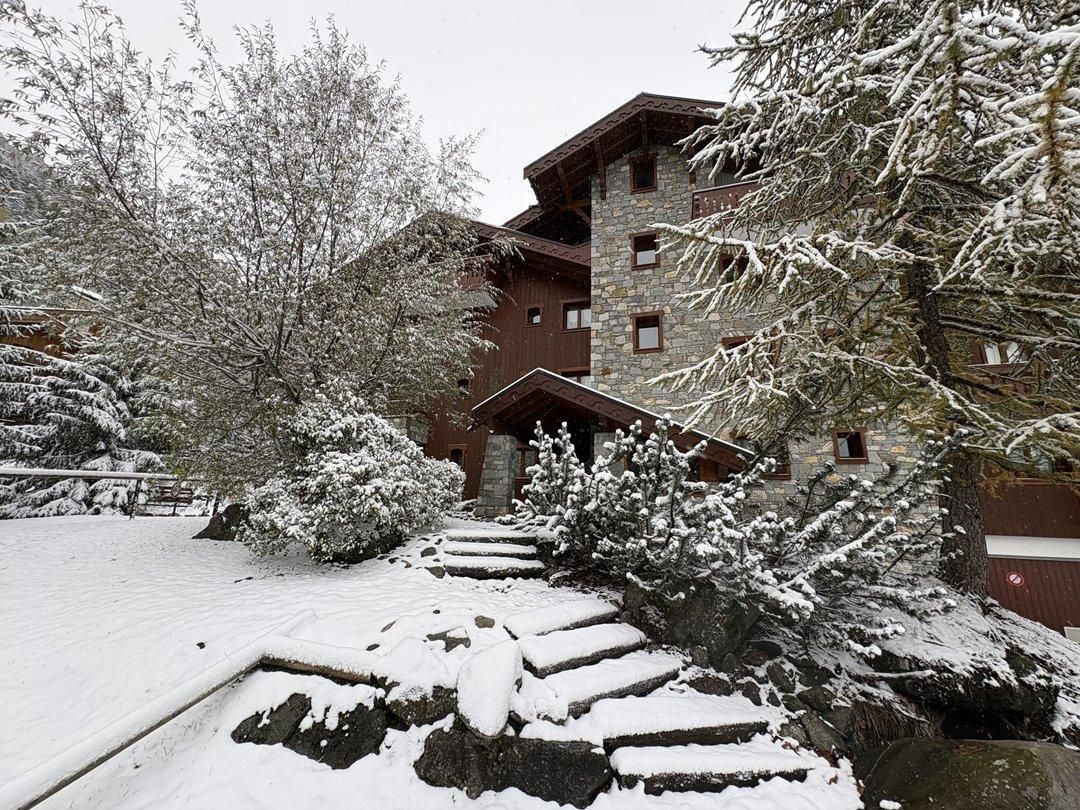 A multi-story building with a stone facade and wooden accents, surrounded by snow-covered trees and a snow-covered pathway leading to the entrance.