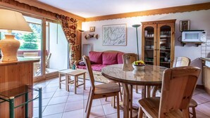A cozy living room with a round glass table, wooden chairs, a pink sofa, and a bookshelf. - 350m from ski slopes, balcony, tv, 40m², Méribel-Mottaret (Méribel - Les Allues)