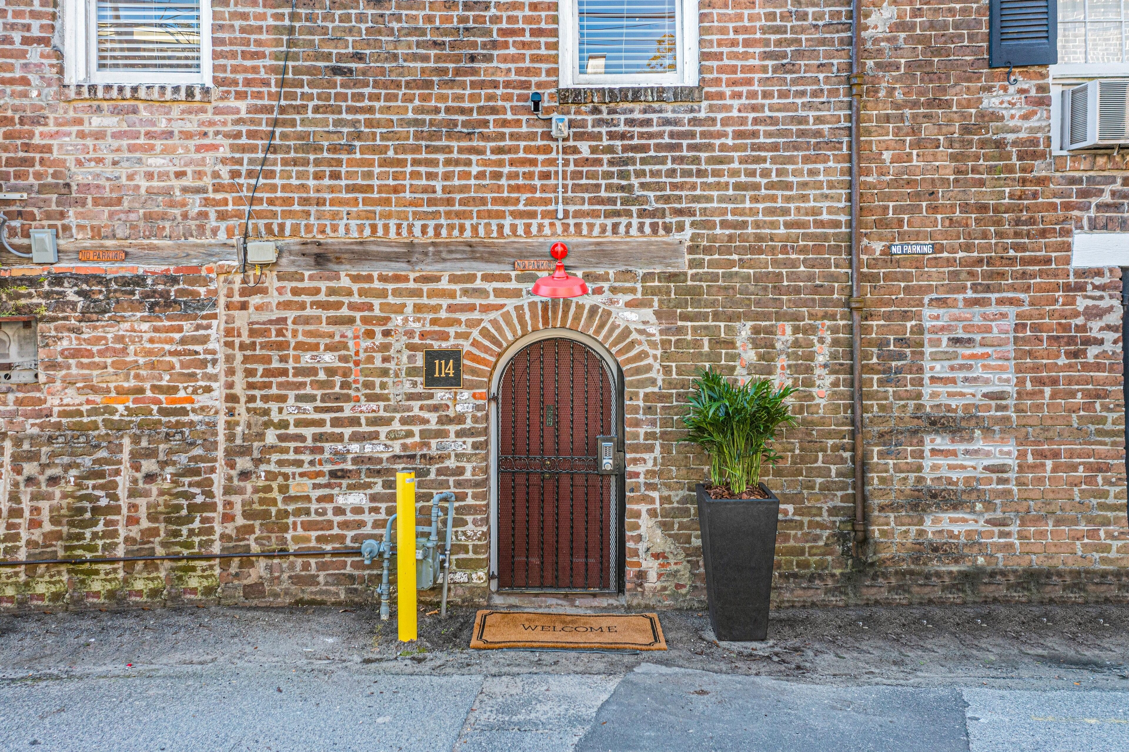Un edificio de ladrillo con una puerta roja, un cartel de 'No Estacionar' y una alfombra de bienvenida.