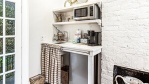 Uma cozinha compacta com micro-ondas, cafeteira e uma pia pequena. Há uma toalha xadrez pendurada na porta, e um cesto perto da pia.
