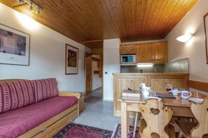 Um quarto aconchegante com teto de madeira, um sofá com almofadas estampadas, uma mesa de jantar com cadeiras e uma área de cozinha com armários de madeira e um micro-ondas.