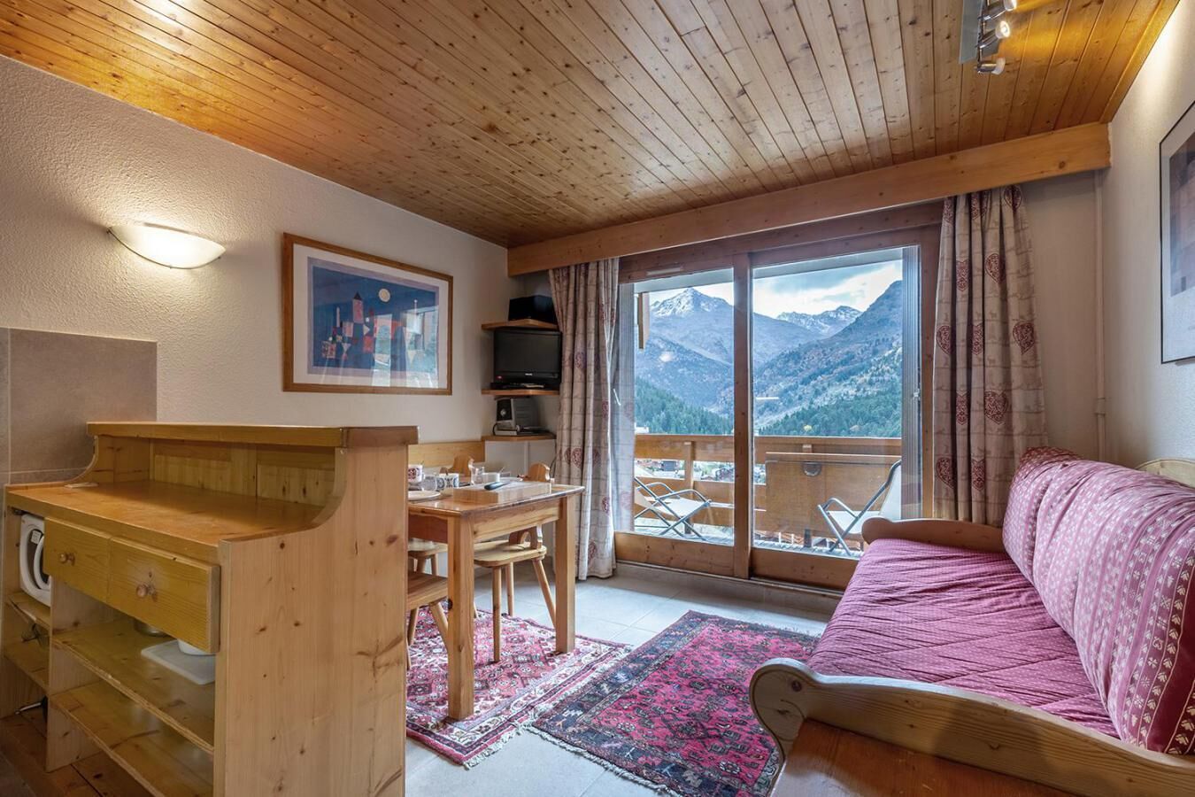 Une pièce chaleureuse avec un bureau en bois, une table à manger, un canapé rose et une grande fenêtre donnant sur une vue imprenable sur les montagnes.