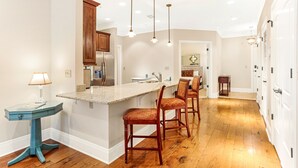 Una cocina con armarios de madera, un refrigerador de acero inoxidable, una encimera de mármol y tres taburetes de bar.
