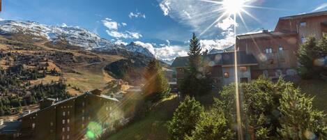 A mountainous landscape with a clear sky, a sun shining, and buildings with visible windows and balconies.
