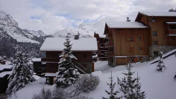 A wooden chalet-style building with multiple balconies, surrounded by snow-covered trees and mountains in the background. - 270m from shops, 3rd floor, balcony, tv, 35m², Méribel-Mottaret (Méribel - Les Allues)