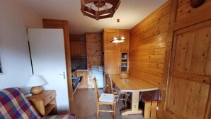 A cozy cabin interior with a wooden dining table, chairs, a sofa, and a kitchen area with cabinets and a refrigerator. - 270m from shops, 3rd floor, balcony, tv, 35m², Méribel-Mottaret (Méribel - Les Allues)