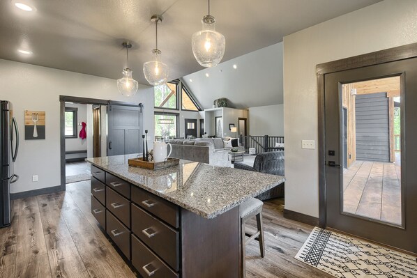 A spacious kitchen with a granite countertop, dark wooden cabinets, and pendant lighting.