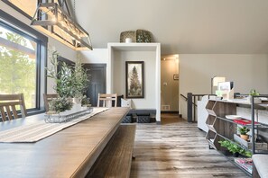 A modern kitchen with a wooden table, chairs, a built-in bench, and a shelving unit with plants.