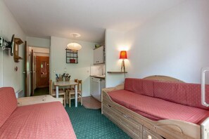 A small, cozy room with two single beds, a wooden dresser, a small table with chairs, a kitchenette, and a red lamp. - 300m from resort center, 7th floor, view mountain, balcony, ski locker, 23m², Méribel-Mottaret (Méribel - Les Allues)