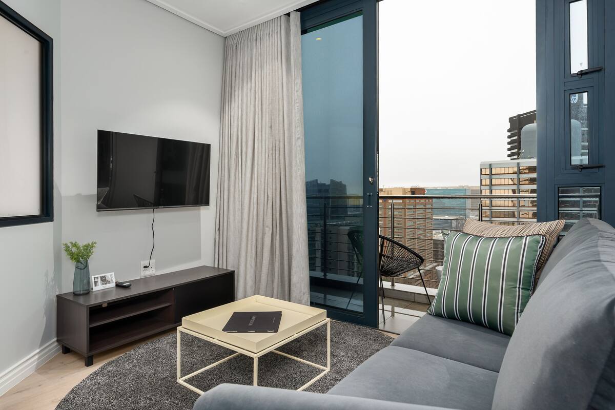 Un salon moderne doté d’un téléviseur à écran plat, d’un canapé, d’une table basse et d’un balcon offrant une vue sur la ville.
