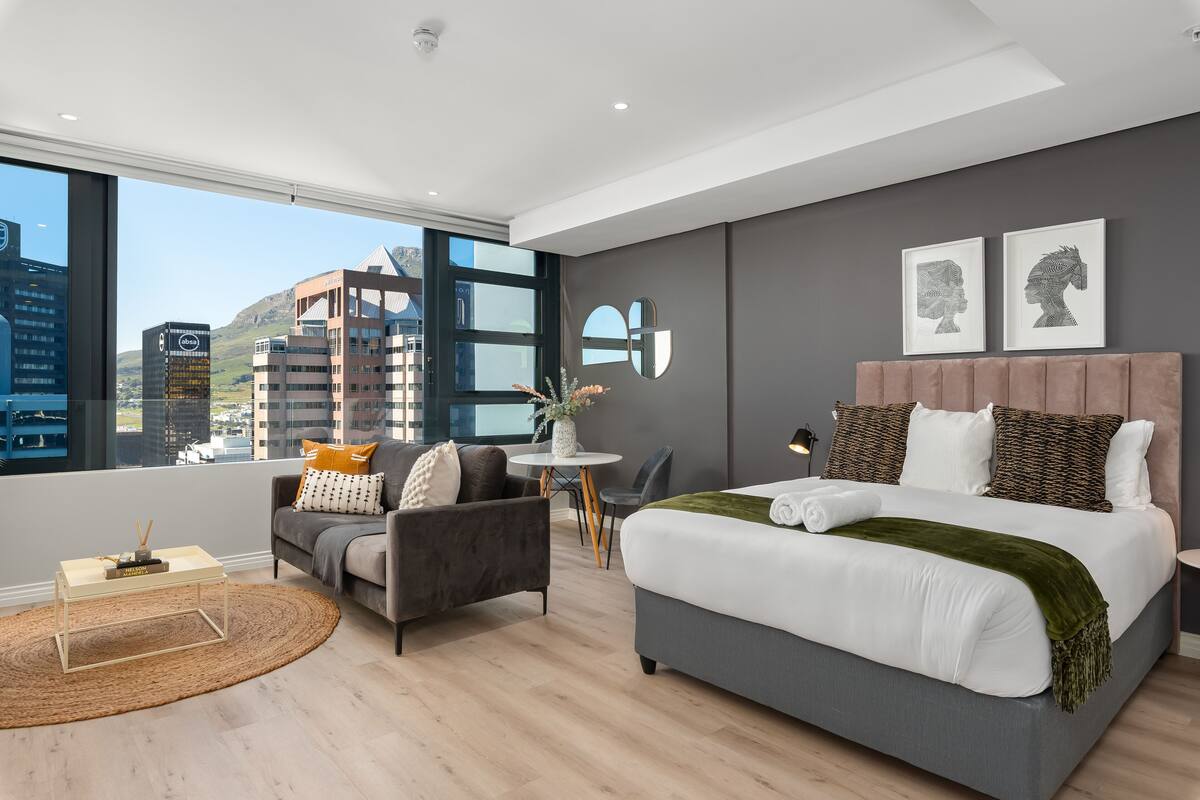 Une chambre d’hôtel moderne, dotée d’un grand lit, d’un canapé, d’une petite table et offrant une vue sur le paysage urbain.