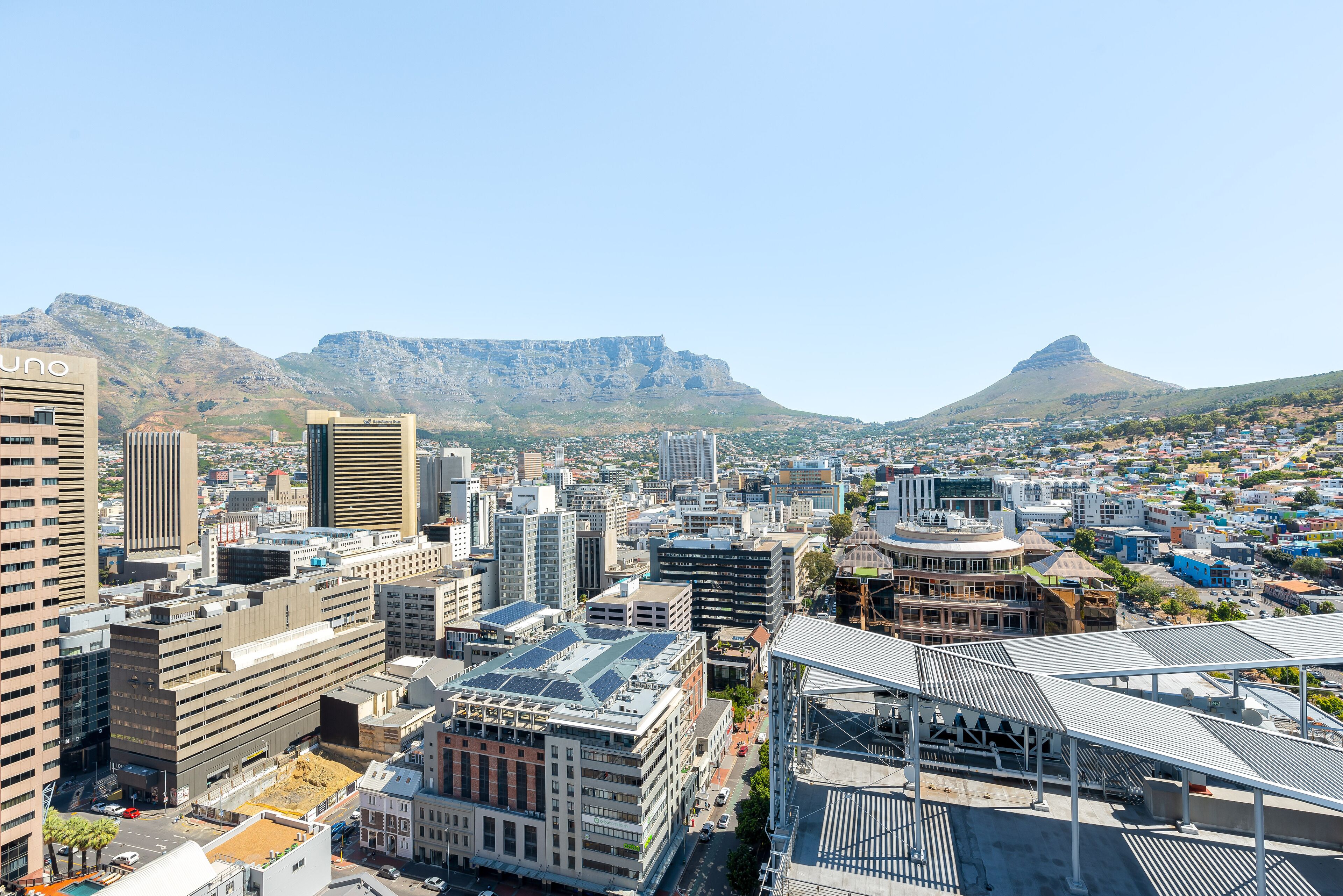 A cityscape with modern buildings, a prominent hotel with a unique roof design, and mountains in the background.