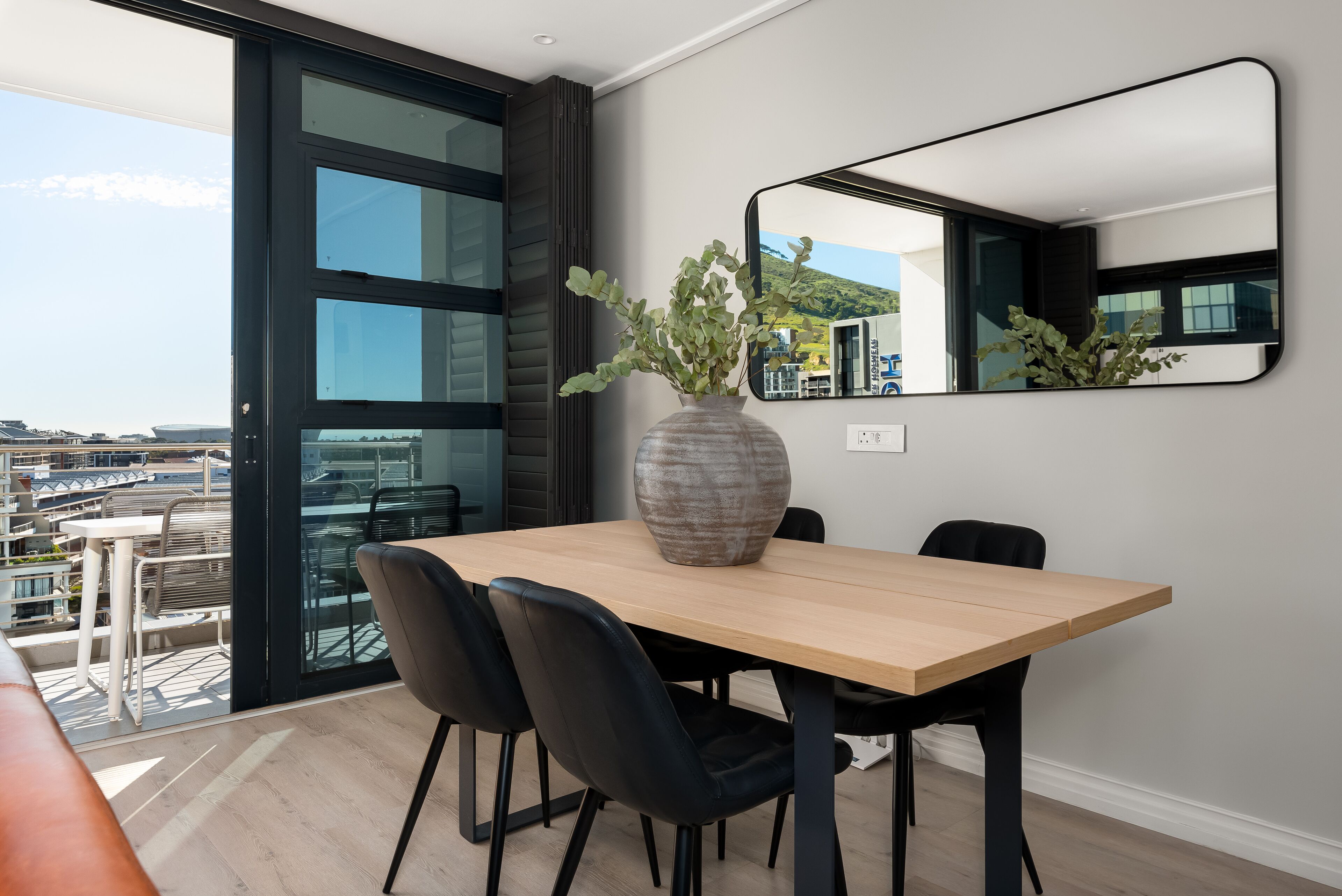 Un espace repas moderne avec une grande table, des chaises noires et un vase rempli de verdure.