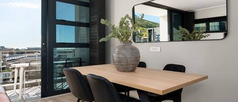 A modern dining area with a large table, black chairs, and a vase of greenery.