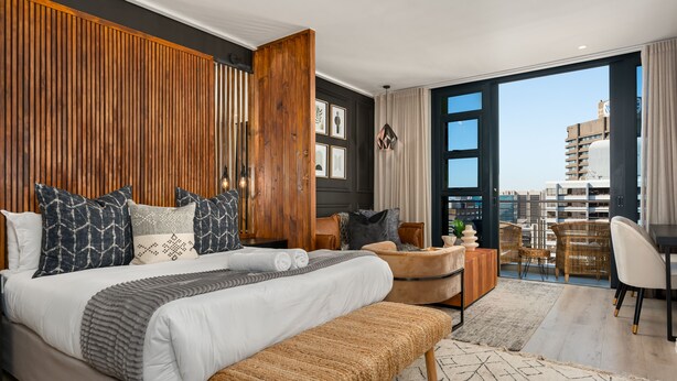 Ein modernes Schlafzimmer mit einem großen Bett, einer Wand aus Holzpaneelen und Blick auf die Stadt vom Balkon aus.