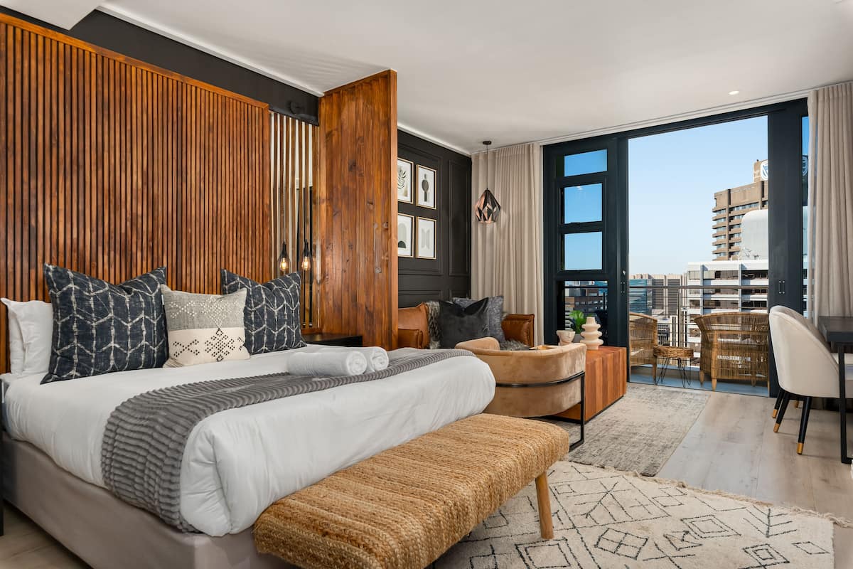 Une chambre moderne avec un grand lit, un mur revêtu de panneaux en bois et une vue sur la ville depuis le balcon.