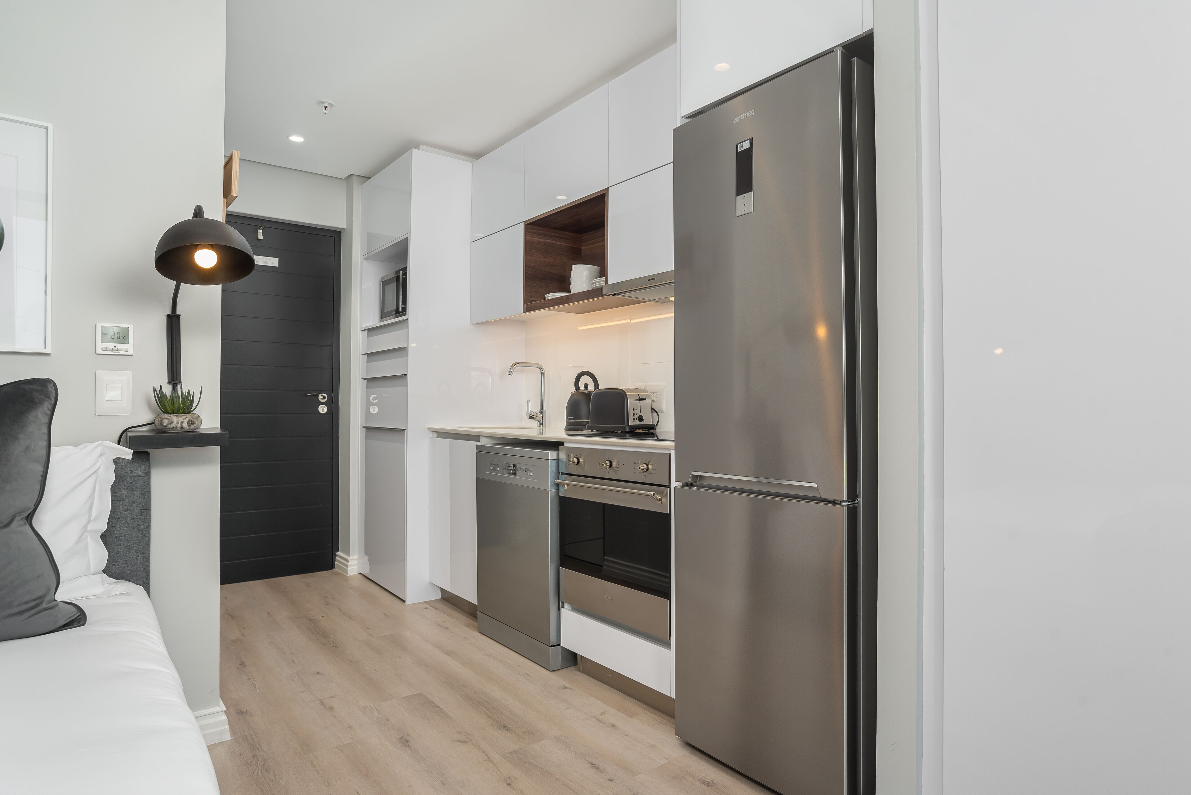 A modern kitchen with white cabinetry, a built-in oven, a dishwasher, and a stainless steel refrigerator.