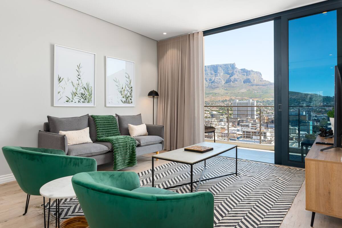 Un salon moderne avec un canapé, des fauteuils verts, une table basse et des œuvres d’art accrochées au mur.
