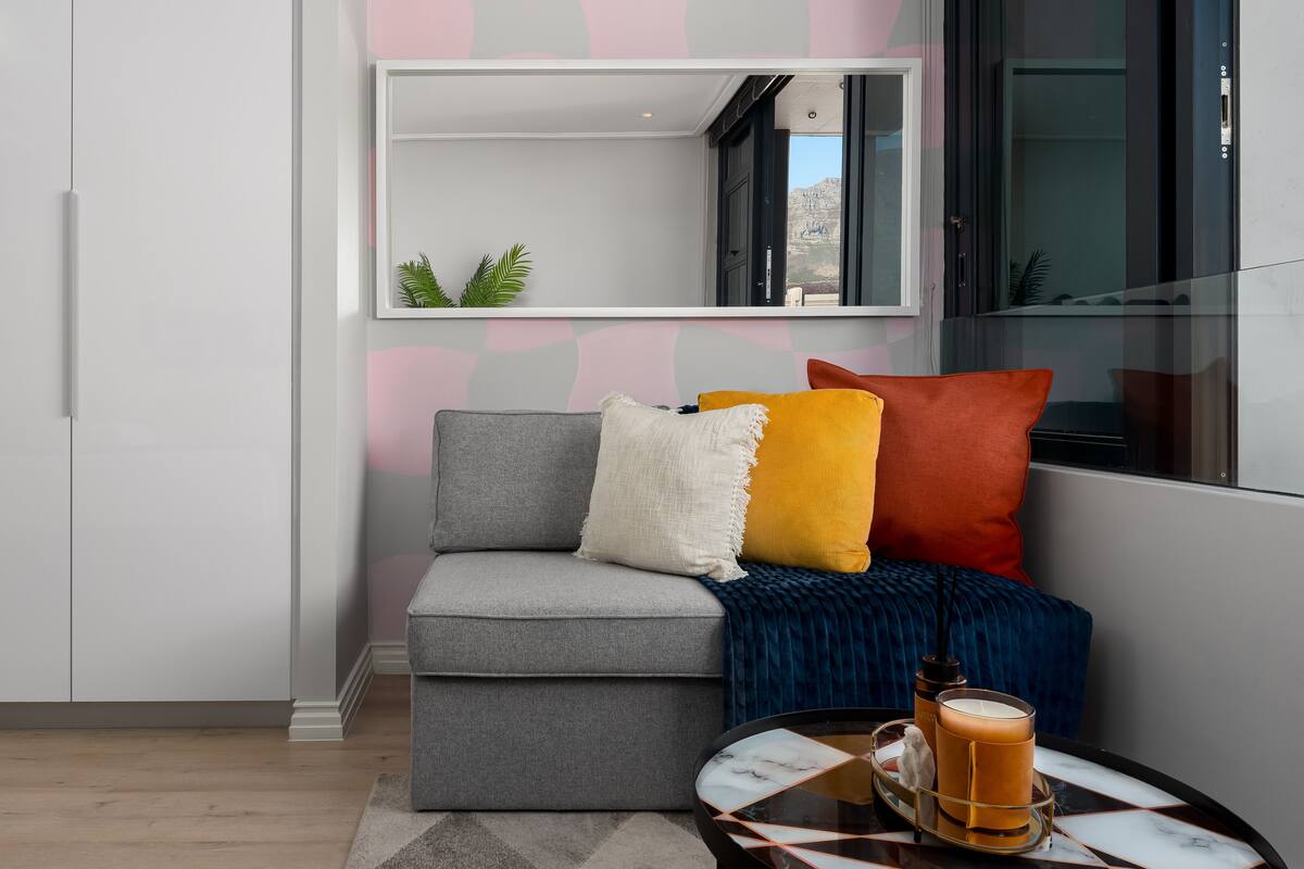 Un salon moderne avec un canapé gris, des coussins colorés, un plaid bleu et une table basse sur laquelle est posée une bougie.