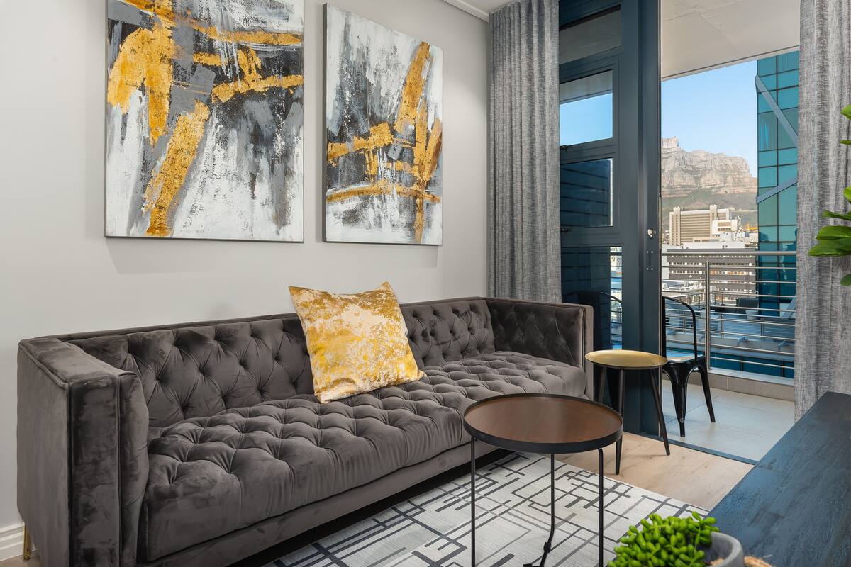 Un salon moderne avec un canapé gris à capitons, une table basse ronde et des tableaux abstraits accrochés au mur.