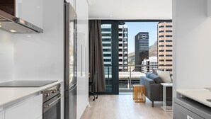 Eine moderne Küche mit Edelstahlgeräten, einem grauen Sofa und Blick auf Stadtgebäude.