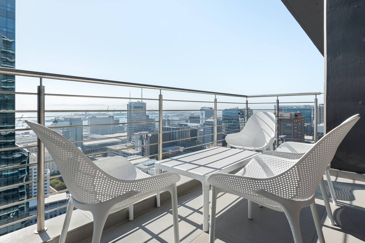 Un balcon avec deux chaises blanches ajourées et une table, offrant une vue sur la ville.