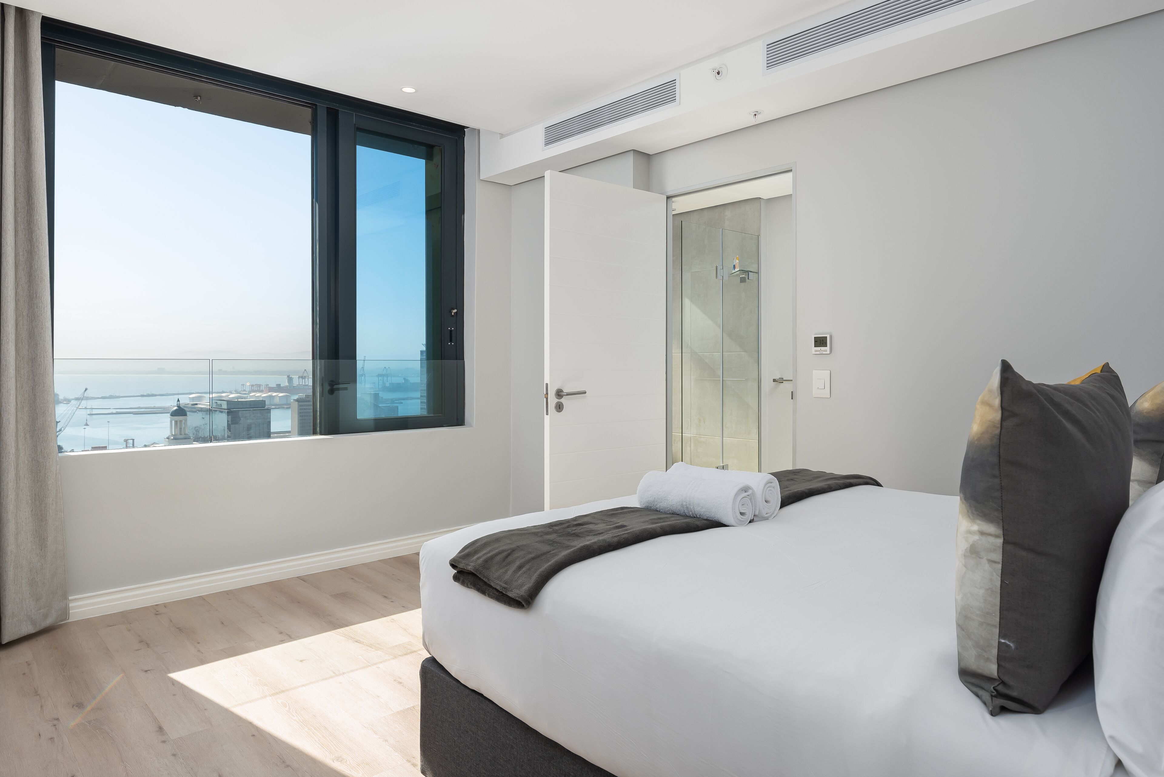 A modern bedroom with a large bed, a glass door leading to a balcony, and a city view.