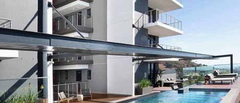 A modern building with a rooftop pool, outdoor seating, and a clear view of the landscape.
