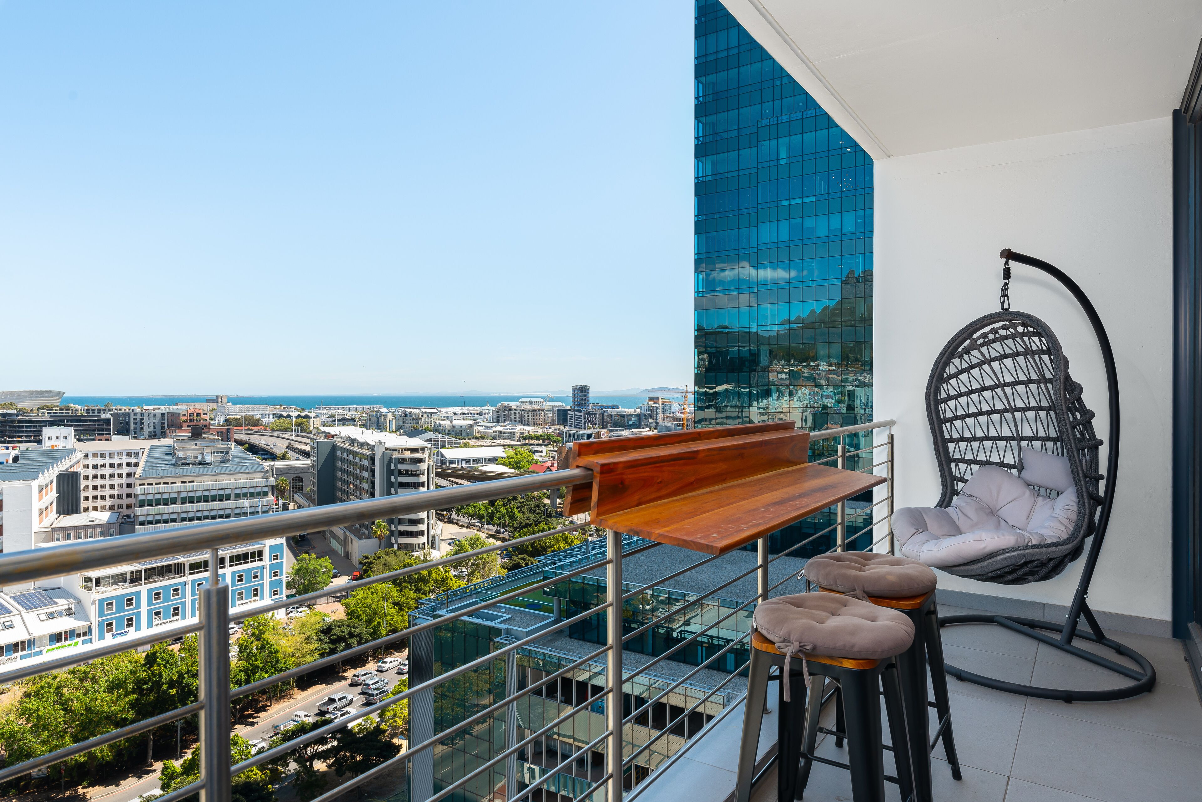 A balcony with a hanging chair, a wooden table, and two bar stools.