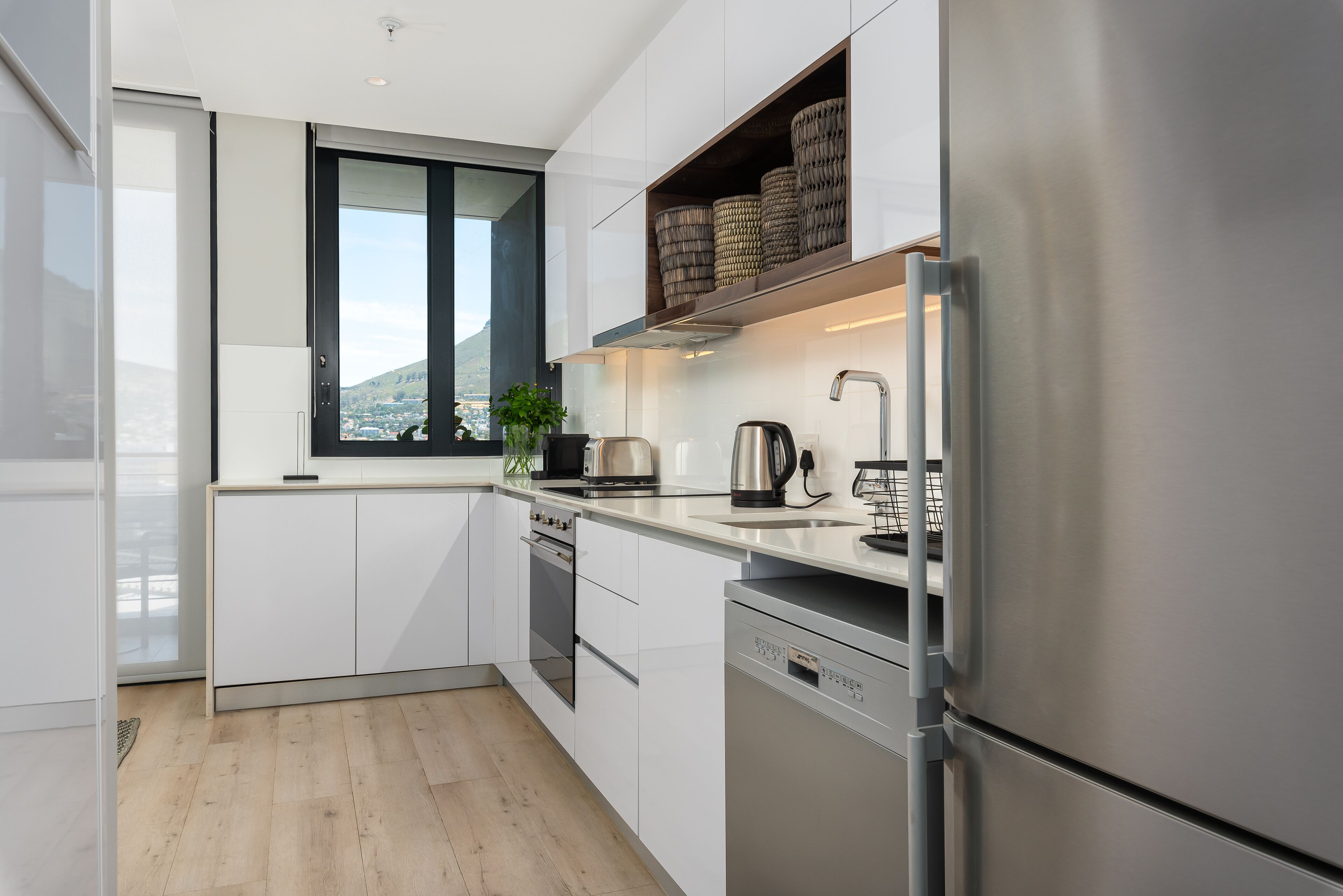 A modern kitchen with white cabinetry, stainless steel appliances, a window with a view, and a plant on the counter.