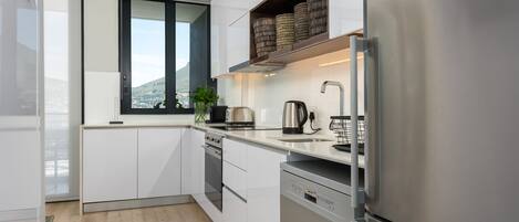 A modern kitchen with white cabinetry, stainless steel appliances, a window with a view, and a plant on the counter.