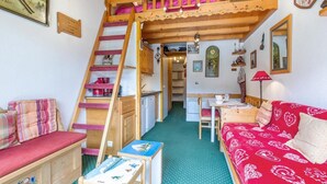 A cozy room with a wooden staircase, a dining area, and a sofa with a red patterned cover. - 90m from ski slopes, 3rd floor, view mountain, balcony, 27m², Méribel-Mottaret (Méribel - Les Allues)