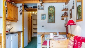 A cozy kitchen with wooden cabinets, a dining area with a red sofa, and a clock on the wall. - 90m from ski slopes, 3rd floor, view mountain, balcony, 27m², Méribel-Mottaret (Méribel - Les Allues)