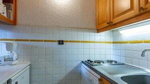 Une cuisine compacte avec des carreaux blancs, une machine à café, un lave-vaisselle et des armoires en bois.