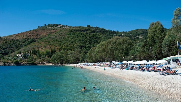 Une plage à l’eau claire, où l’on peut voir des gens se baigner et des parasols installés sur le sable.